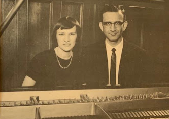 two ancestors sit side by side behind an open piano 